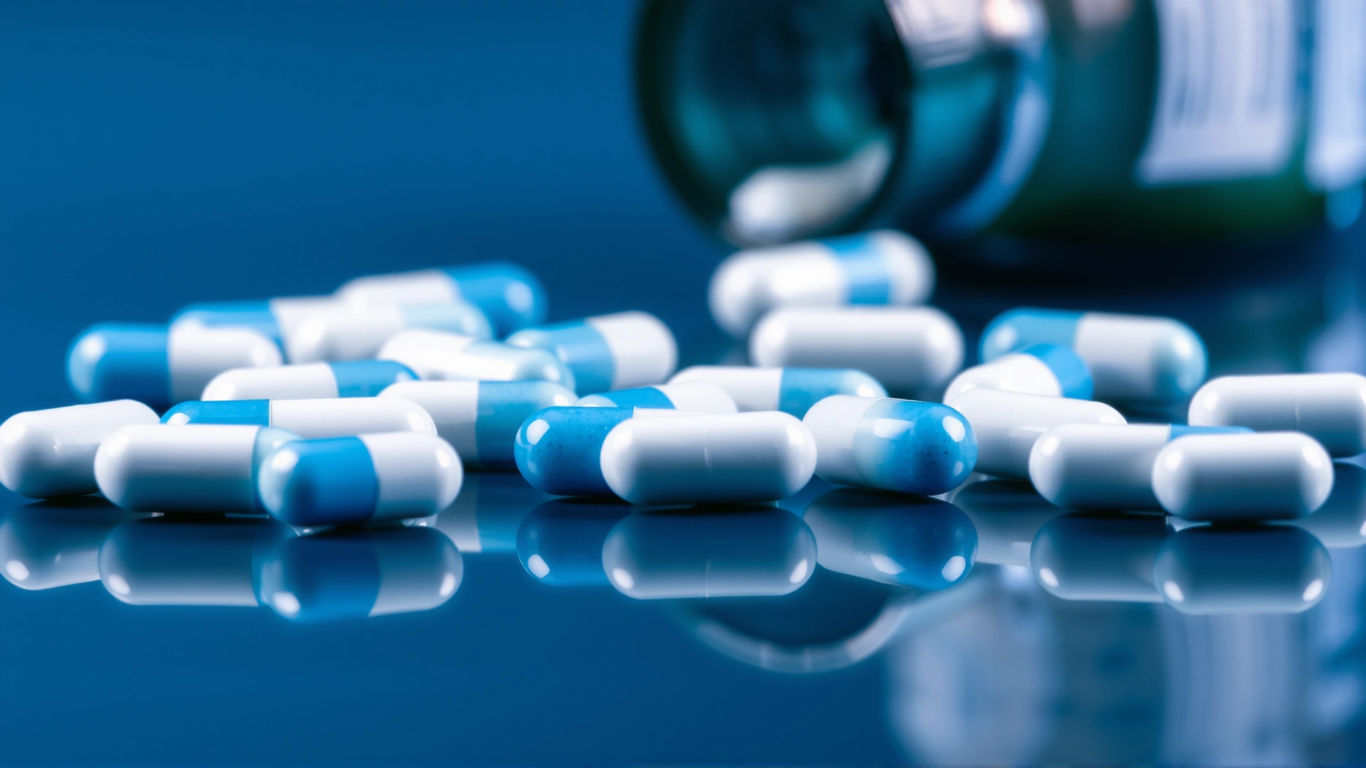 Macro shot of white and blue Prazosin capsules scattered on a reflective surface with a blurred prescription bottle in the background