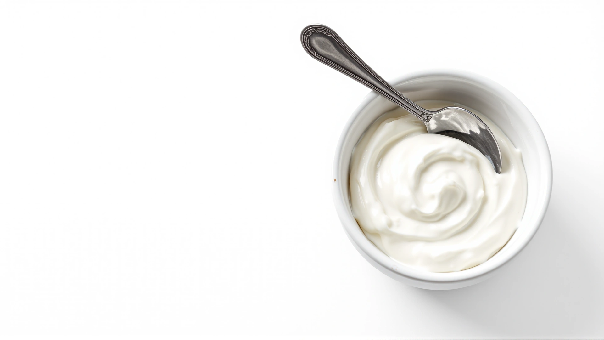 Bowl of plain Greek yogurt with a silver spoon on a clean white background