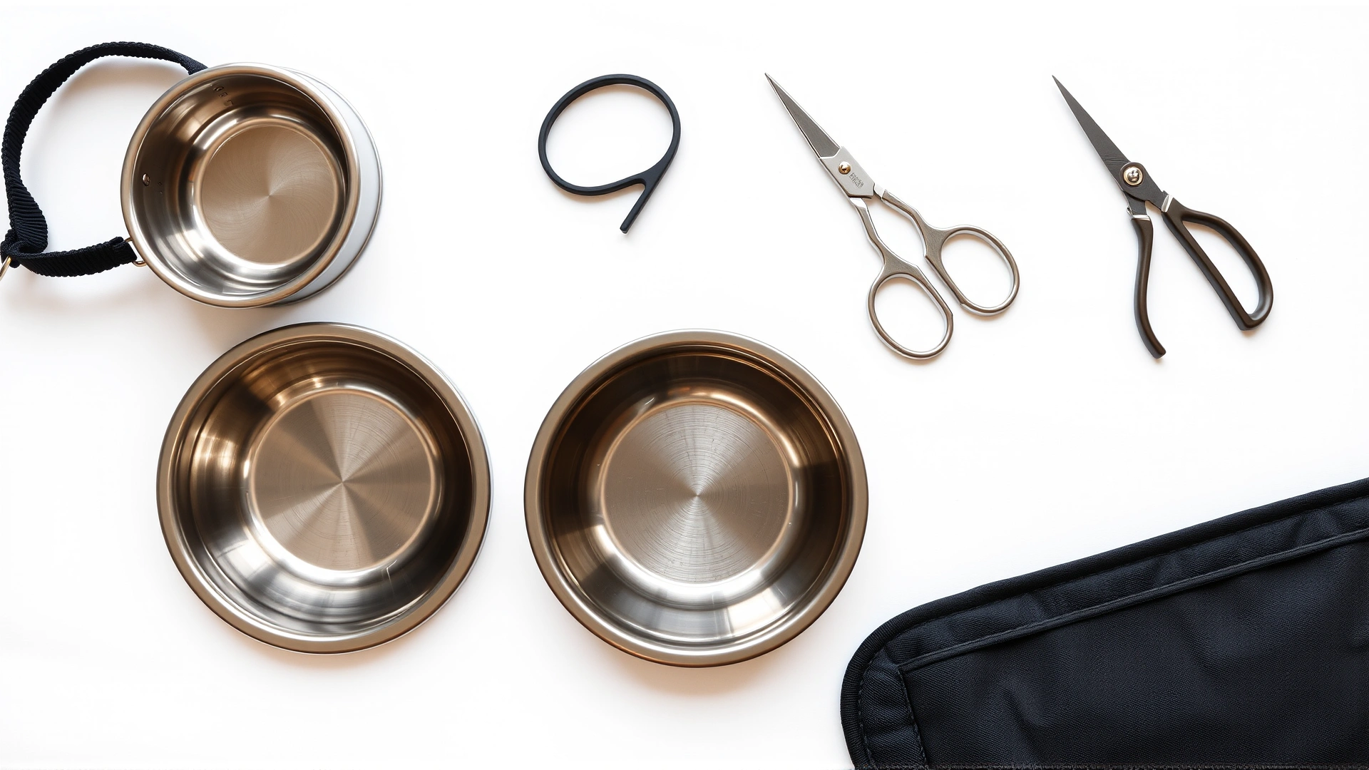 Flat lay on white background of clean stainless steel bowls, nylon collar, grooming scissors and a portable pet crate door, all looking spotless.
